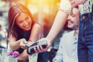 Merchant cash advance concept. Smiling woman tapping credit card against card reader outside restaurant