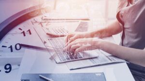 Woman typing overlaid by clock face, reduce staff hours concept